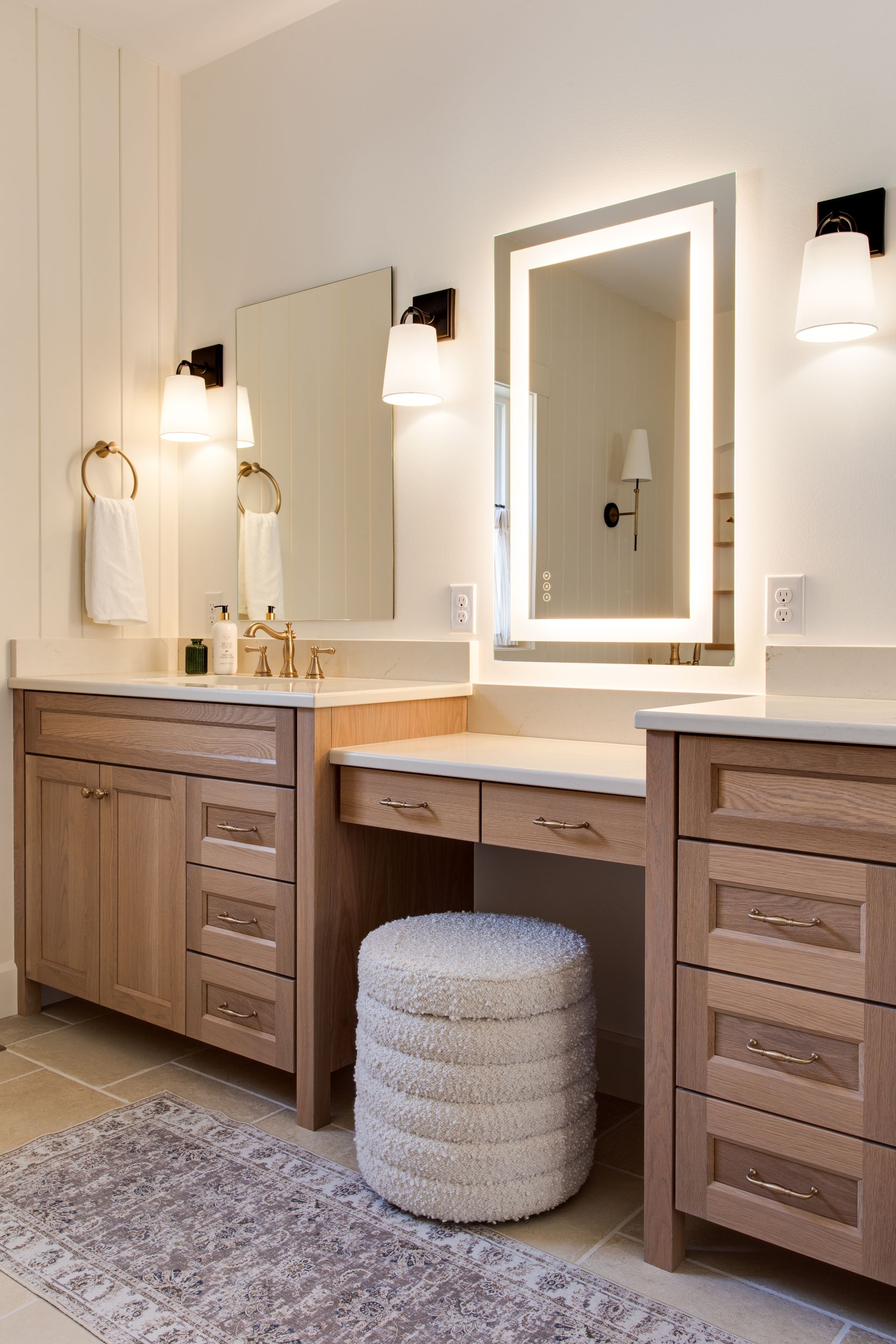 A bathroom with two sinks , two mirrors and a stool.