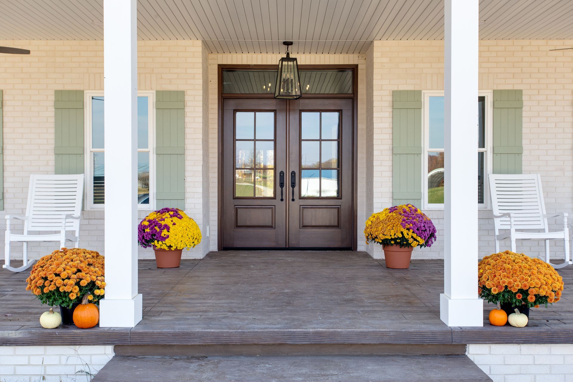 A porch decorated for fall with pumpkins and flowers.