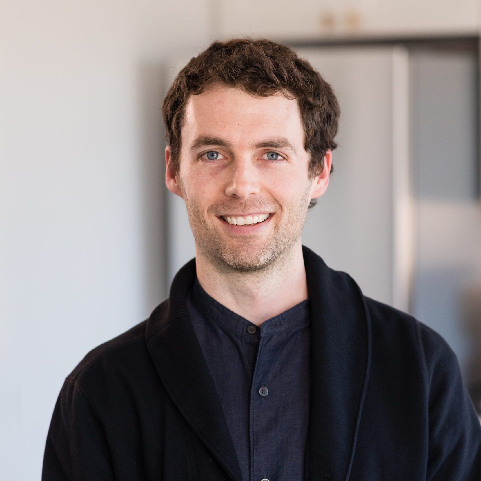 A man wearing a black jacket and a black shirt is smiling for the camera.