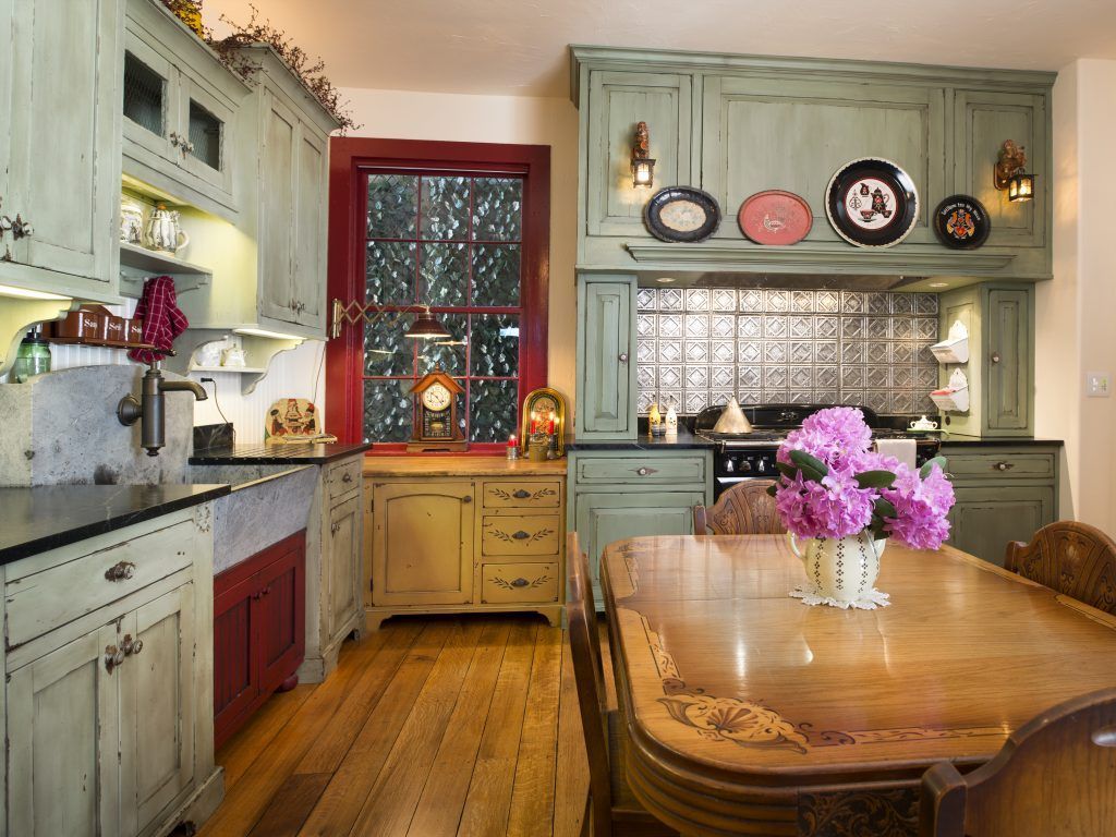 A kitchen with green cabinets and a table with a vase of flowers on it.
