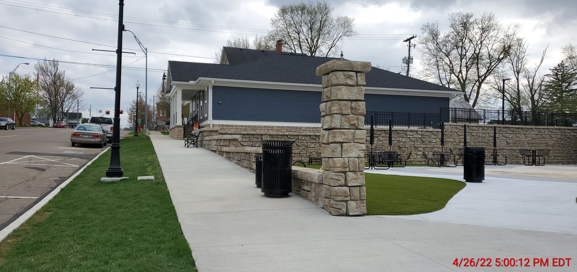 A sidewalk leading to a house with a black trash can in front of it
