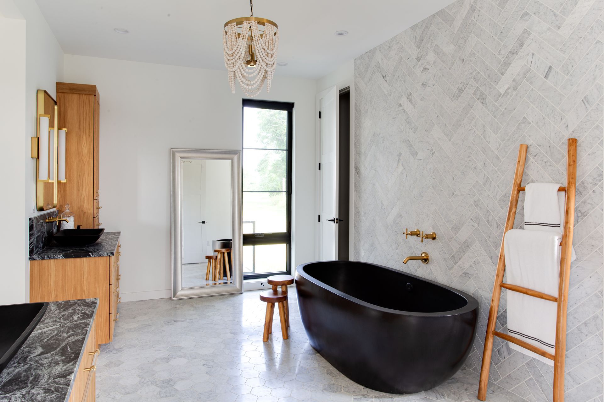 A bathroom with a black tub, sink, mirror and ladder.