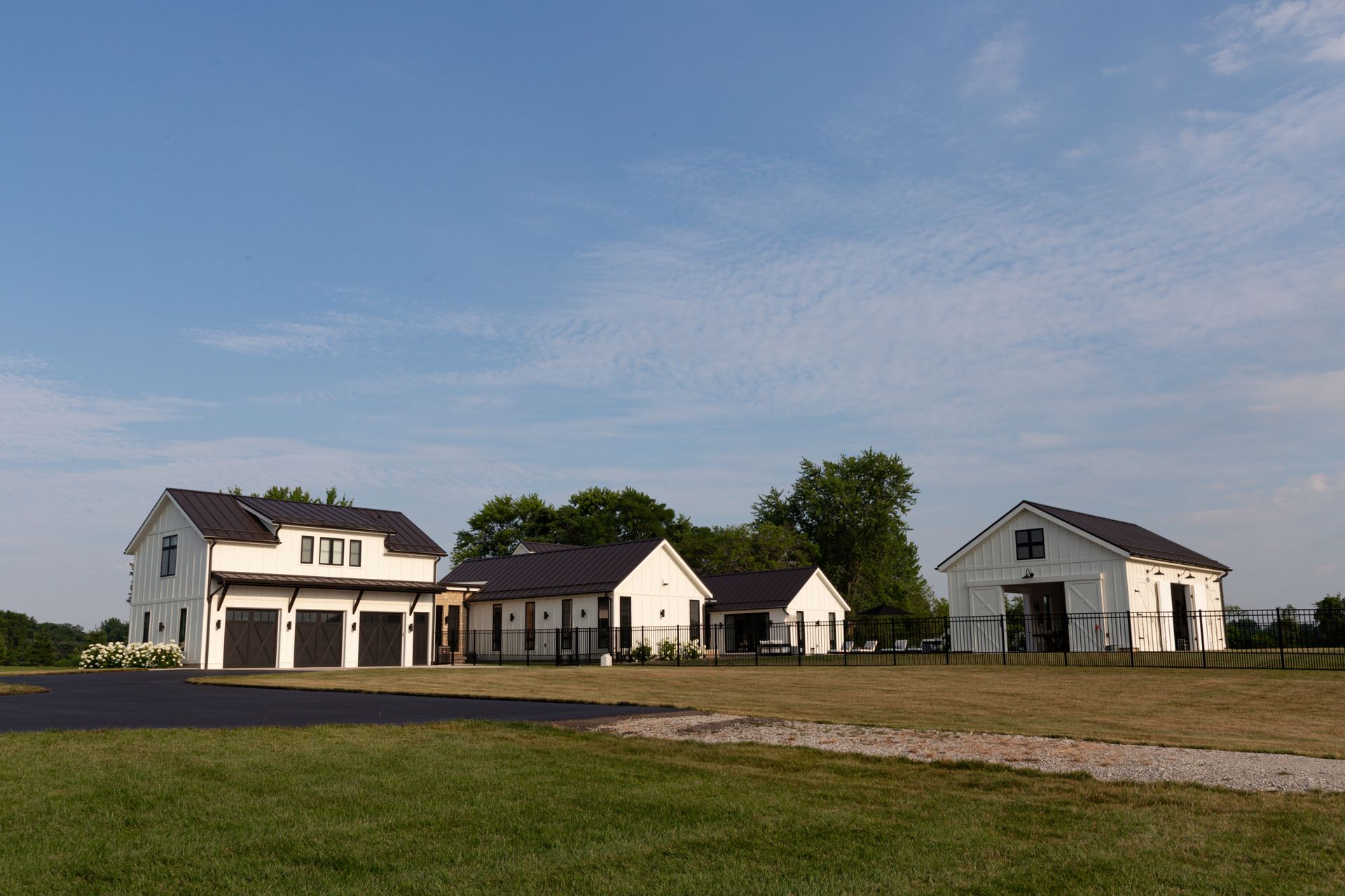 A white house with a black roof is sitting in the middle of a grassy field.