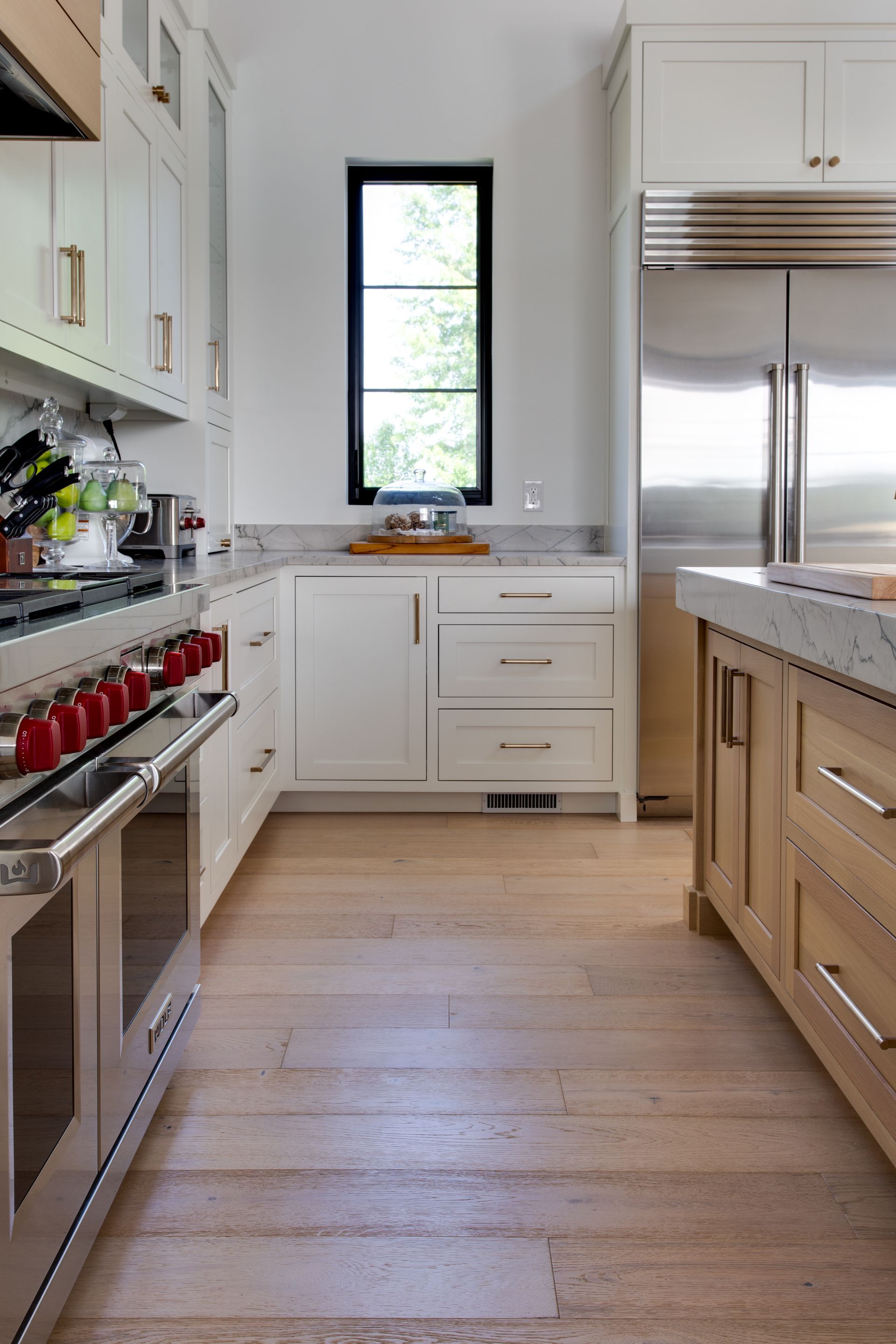 A kitchen with white cabinets , stainless steel appliances , wooden floors and a window.