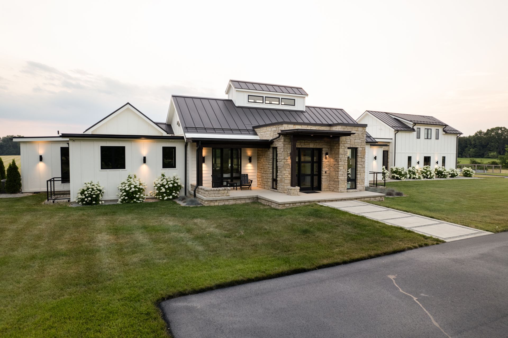 A large white house with a gray roof is sitting on top of a lush green field.