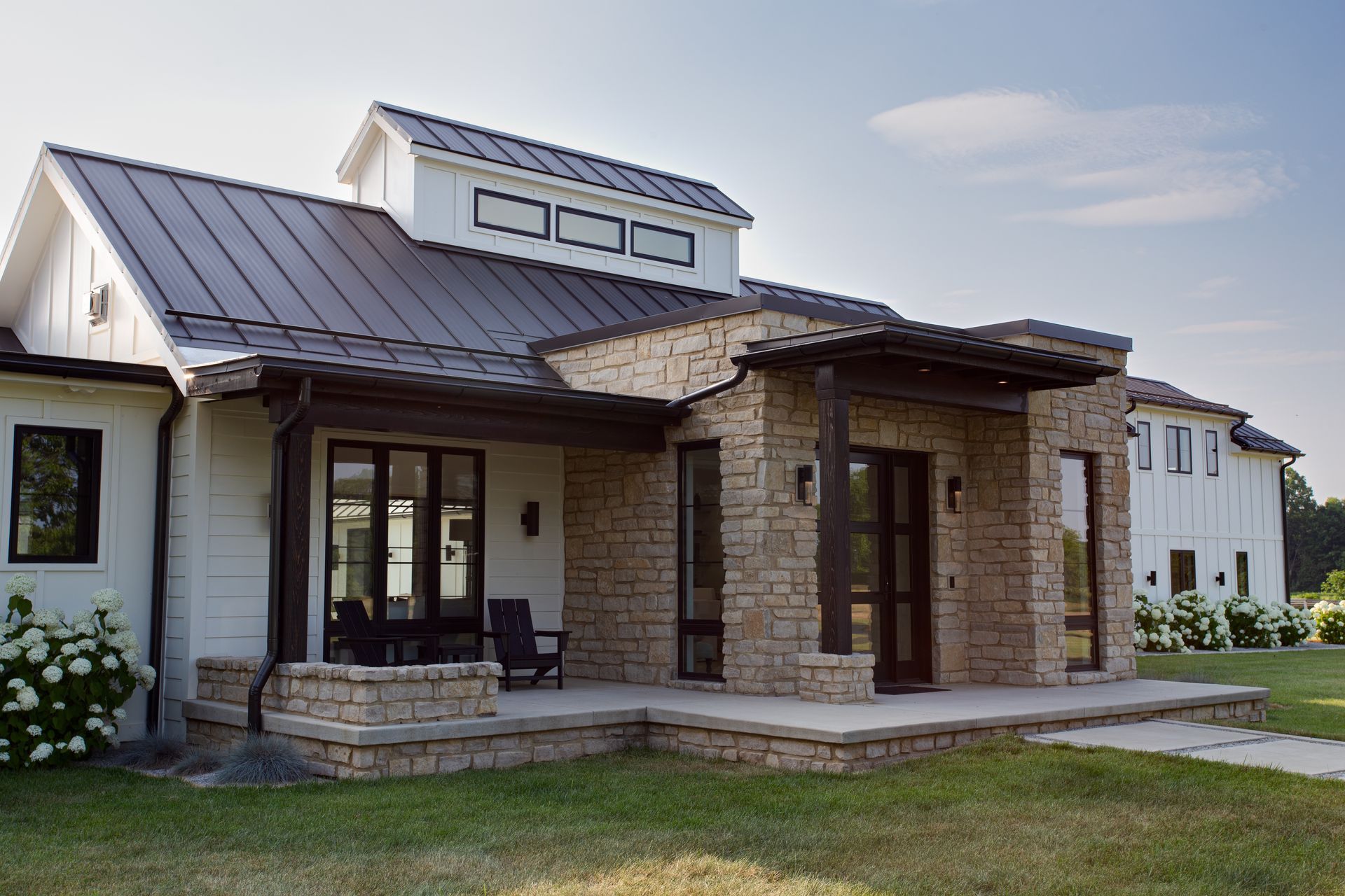 A white house with a metal roof and a stone wall is sitting on top of a lush green field.