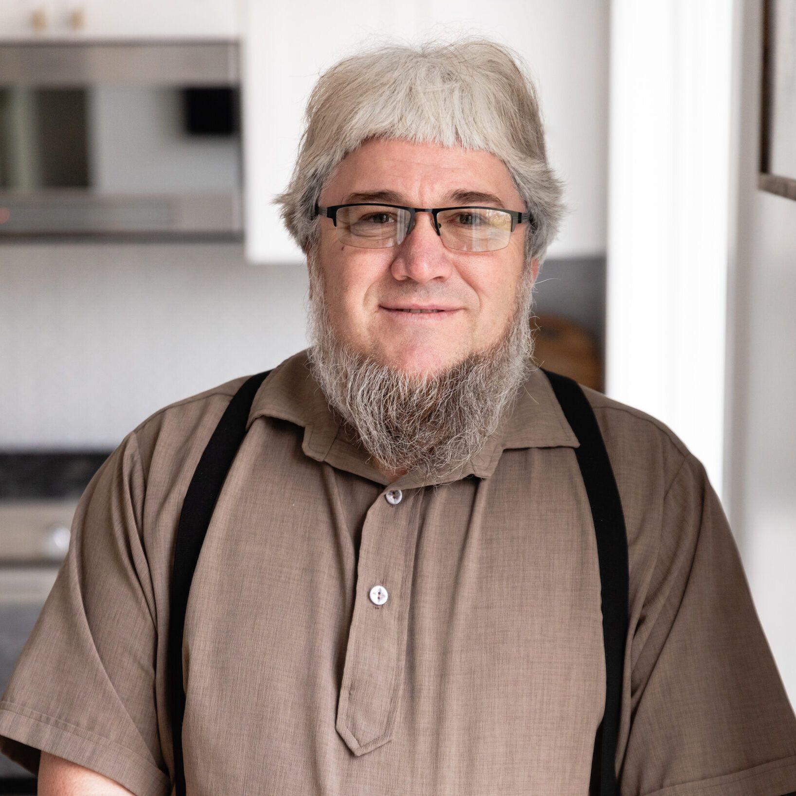 A man with a beard wearing suspenders and glasses.