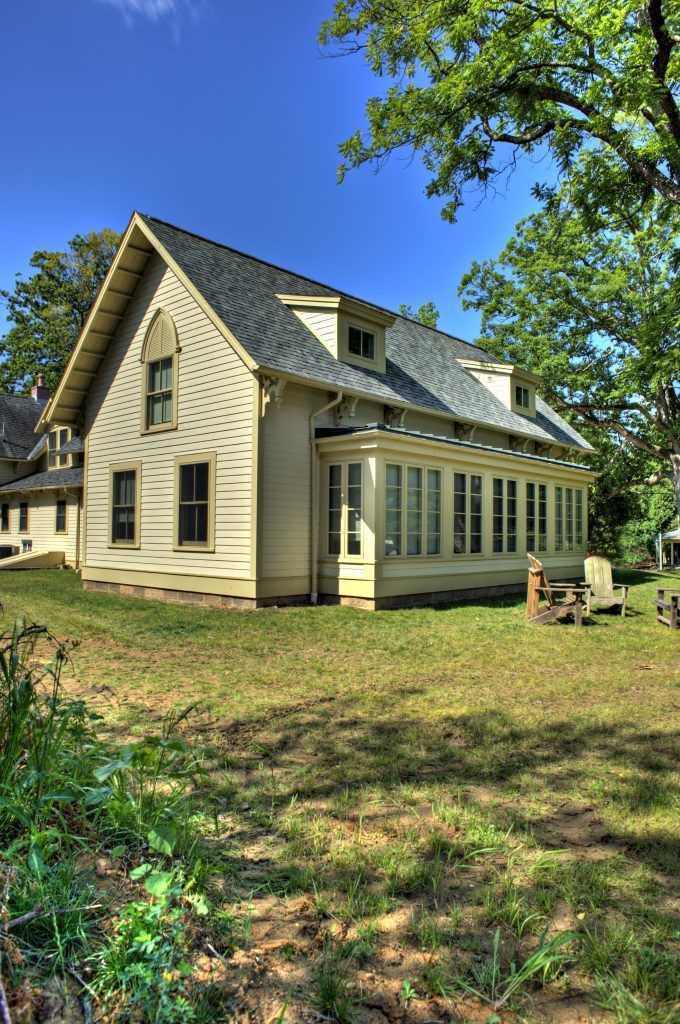 A large house with a gray roof sits in the middle of a lush green field.