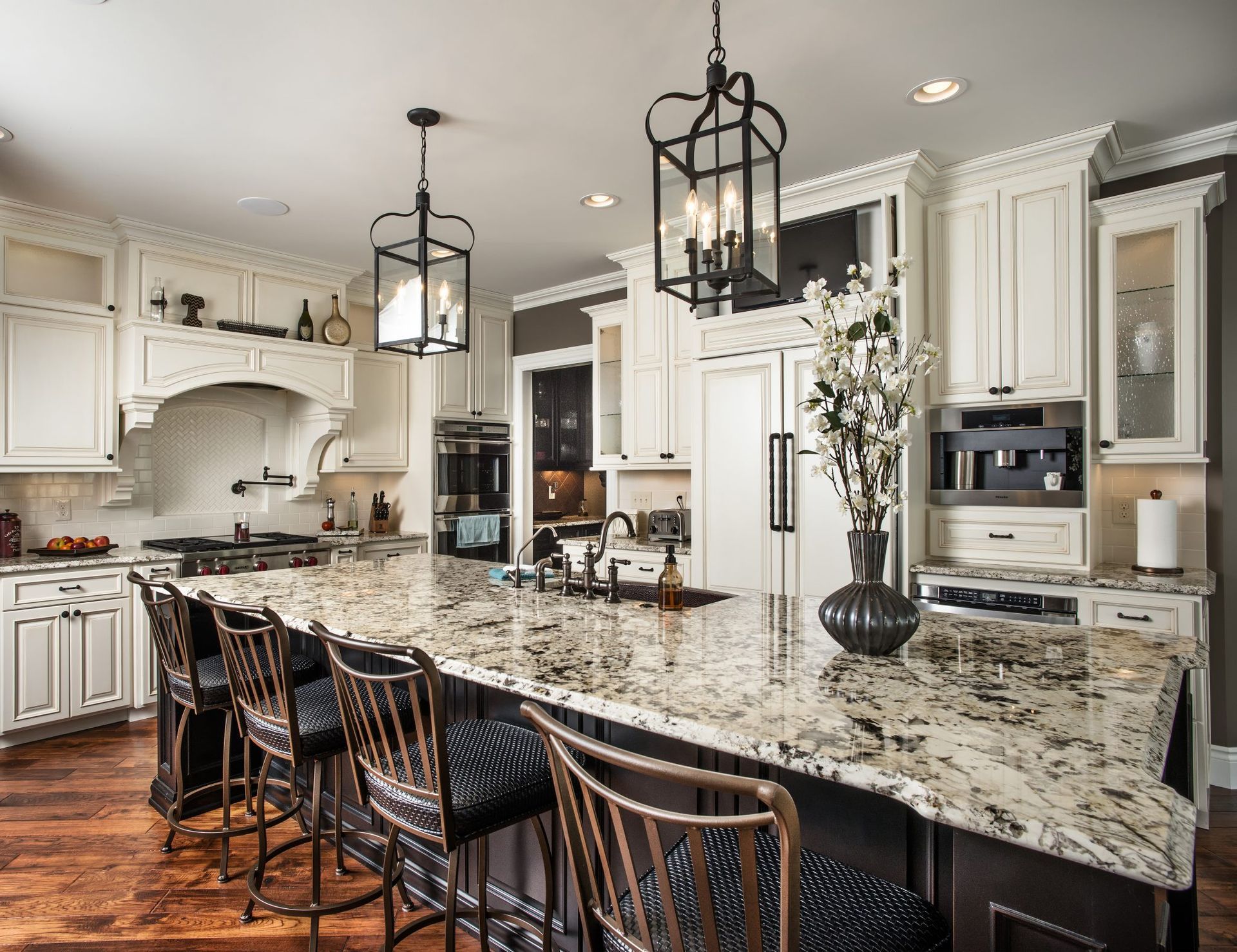 A kitchen with white cabinets , granite counter tops , stools and a large island.