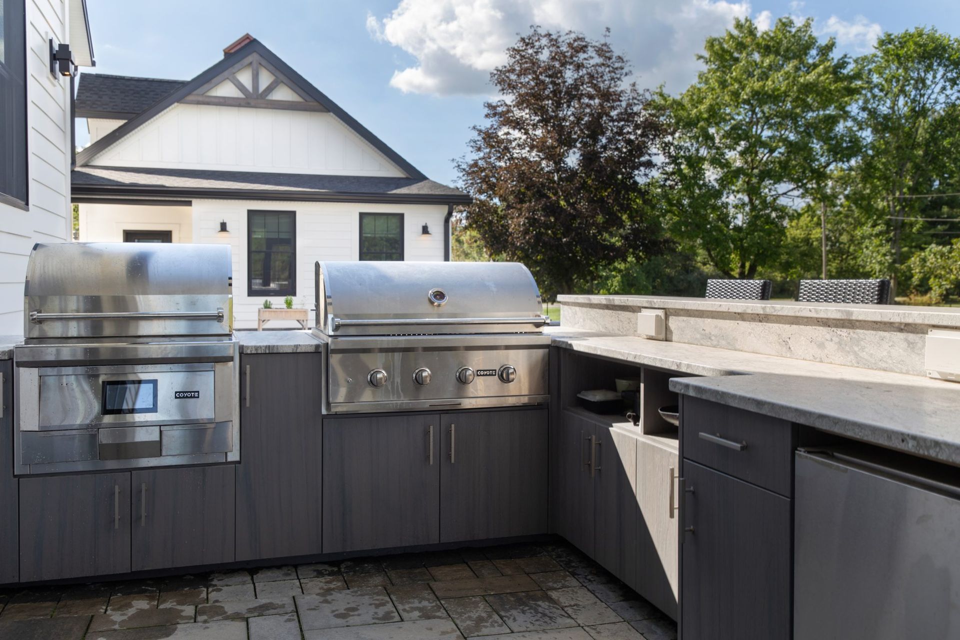 An outdoor kitchen with a grill and a sink in front of a house.