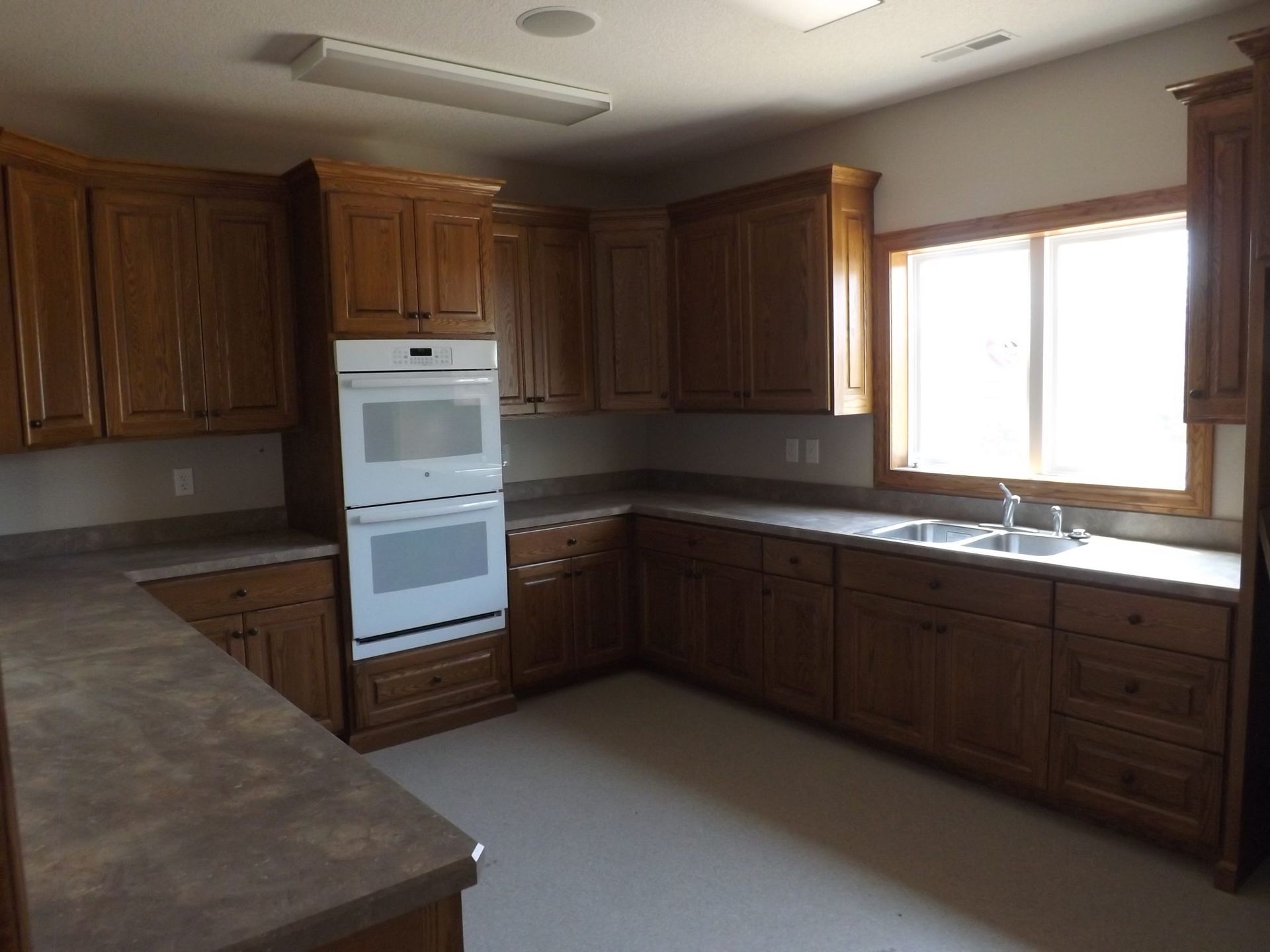 An empty kitchen with wooden cabinets and white counter tops.