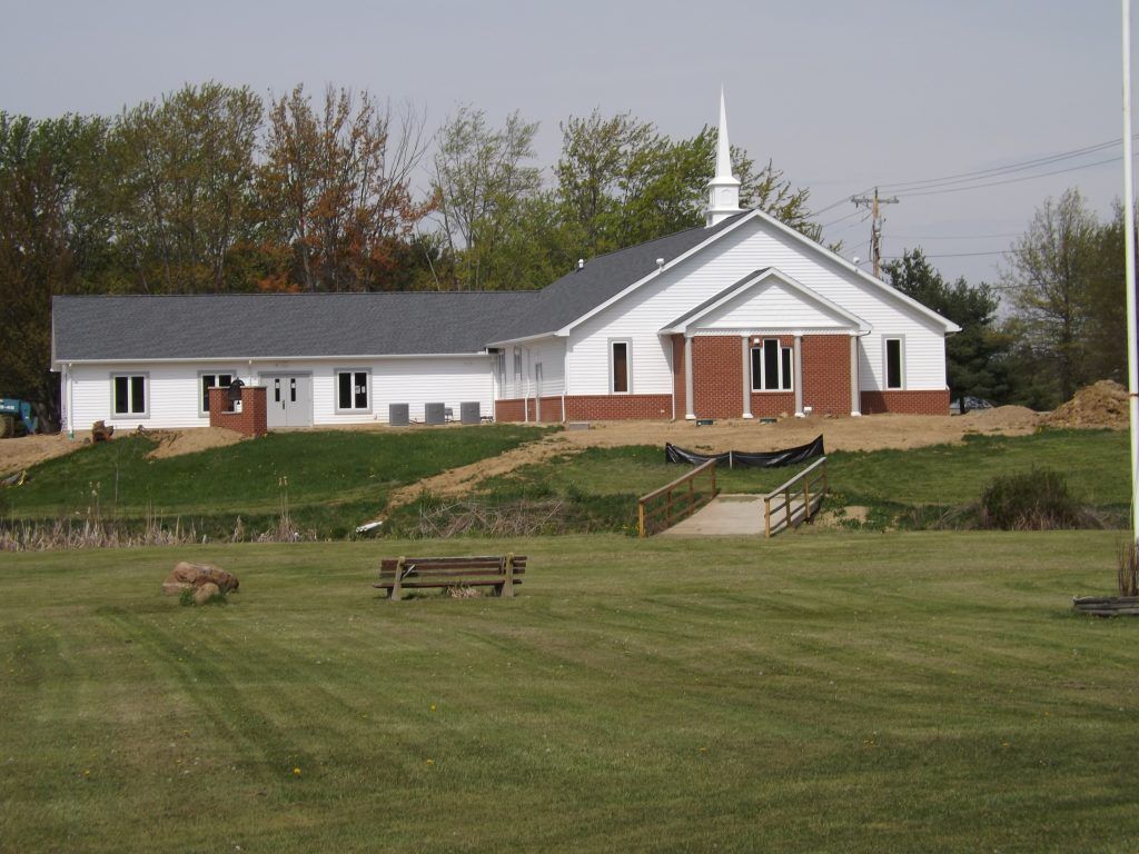 A white church with a steeple sits in the middle of a grassy field.