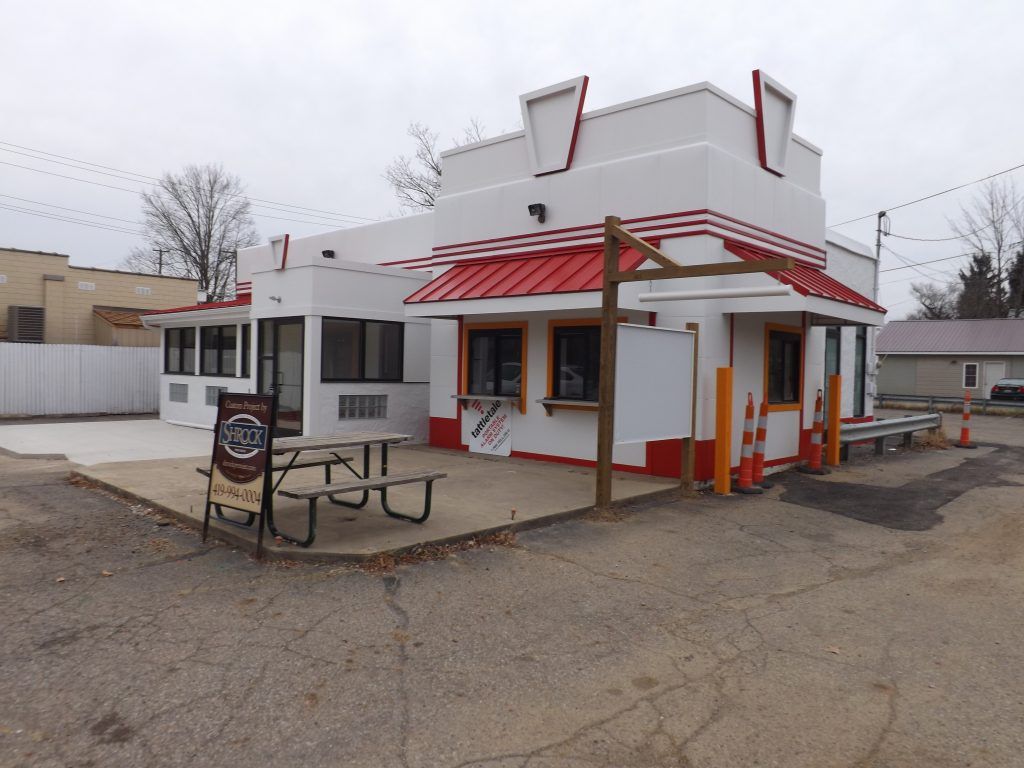 A white building with a red roof and a picnic table in front.