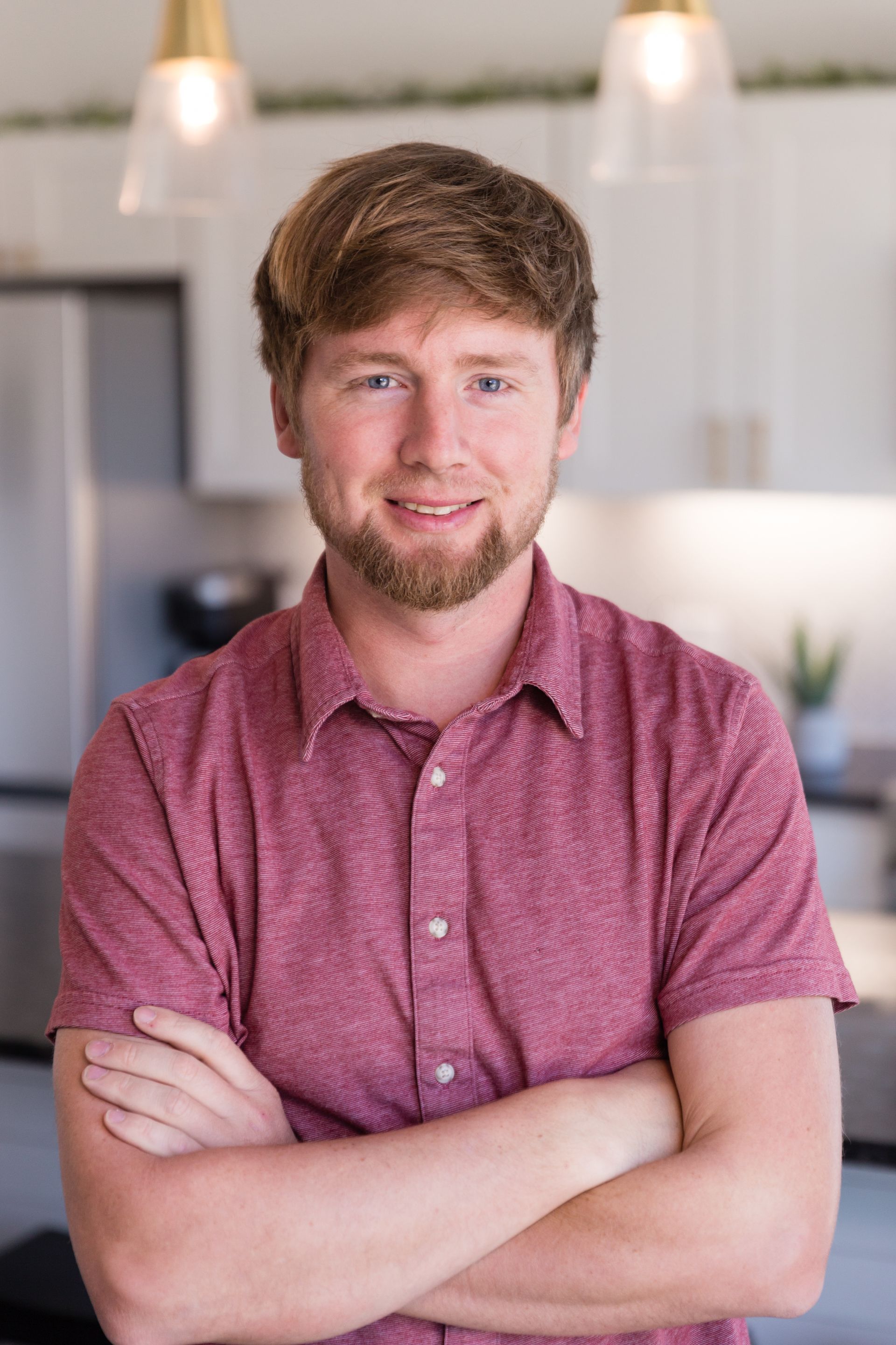 A man in a red shirt is standing with his arms crossed in a kitchen.