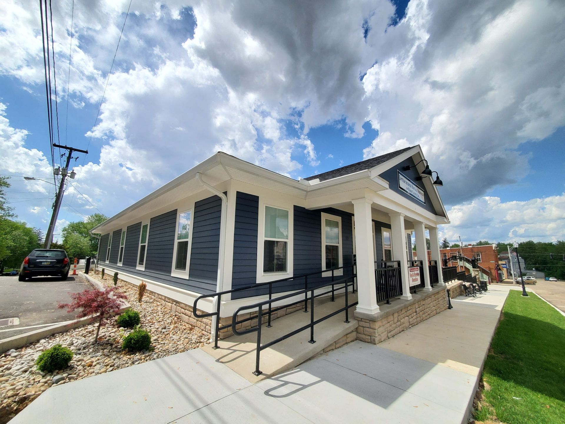 A blue and white house with a porch and a car parked in front of it.