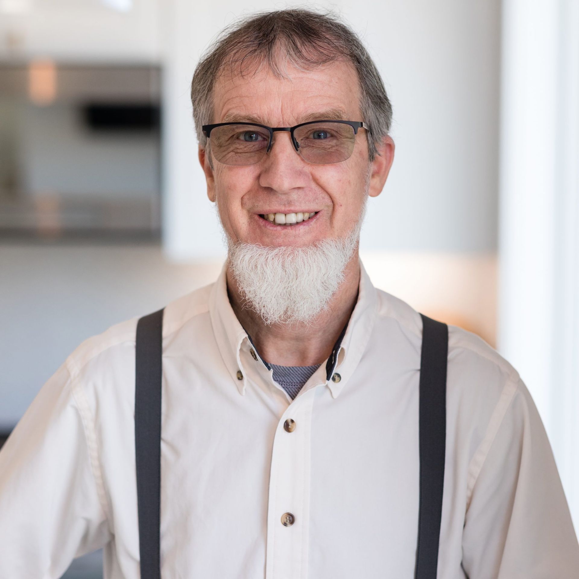 A man with a beard and suspenders is smiling for the camera.