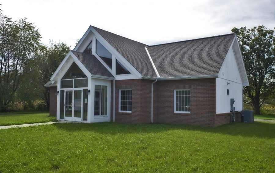 A brick house with a white trim sits in the middle of a lush green field.