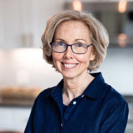 A woman wearing glasses and a blue shirt is smiling for the camera.