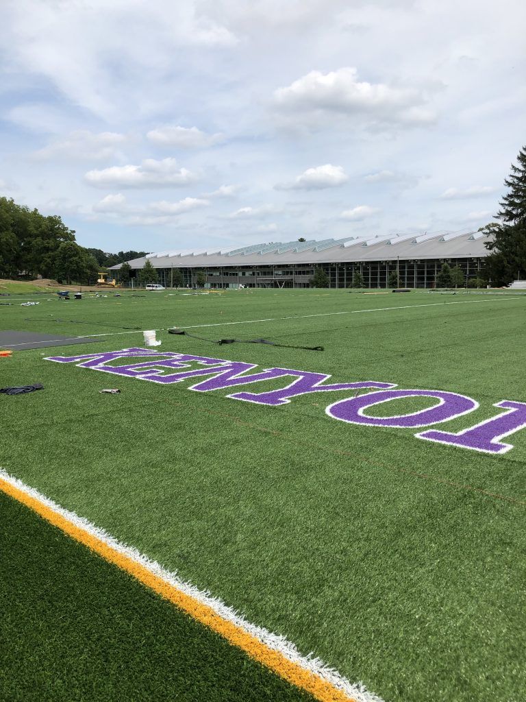 A football field with purple and white letters on it and a building in the background.