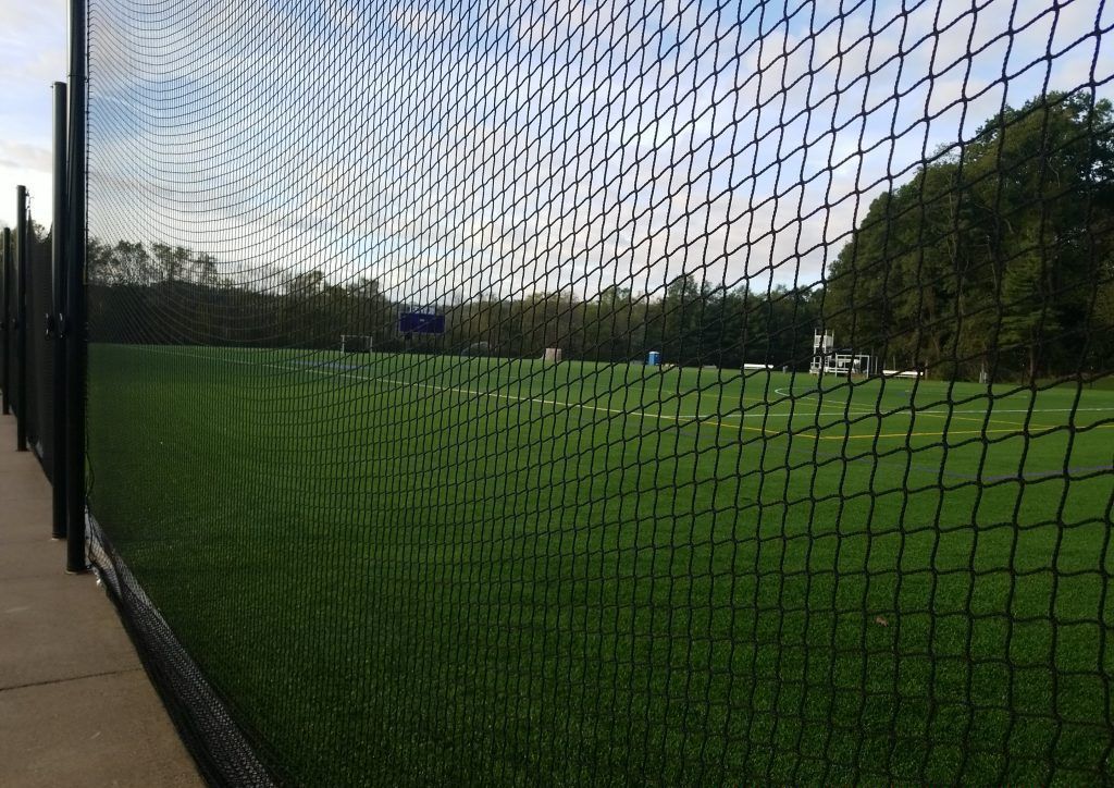 A fence surrounds a soccer field with trees in the background.
