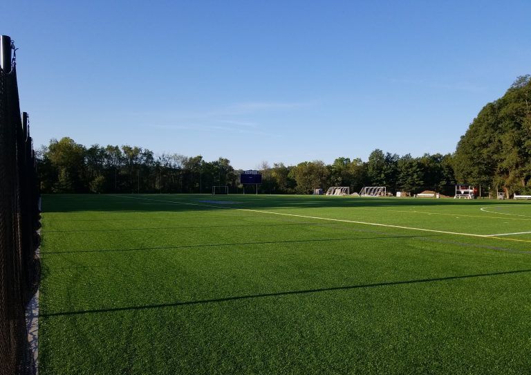 A football field with a fence in the foreground and a blue sky in the background.