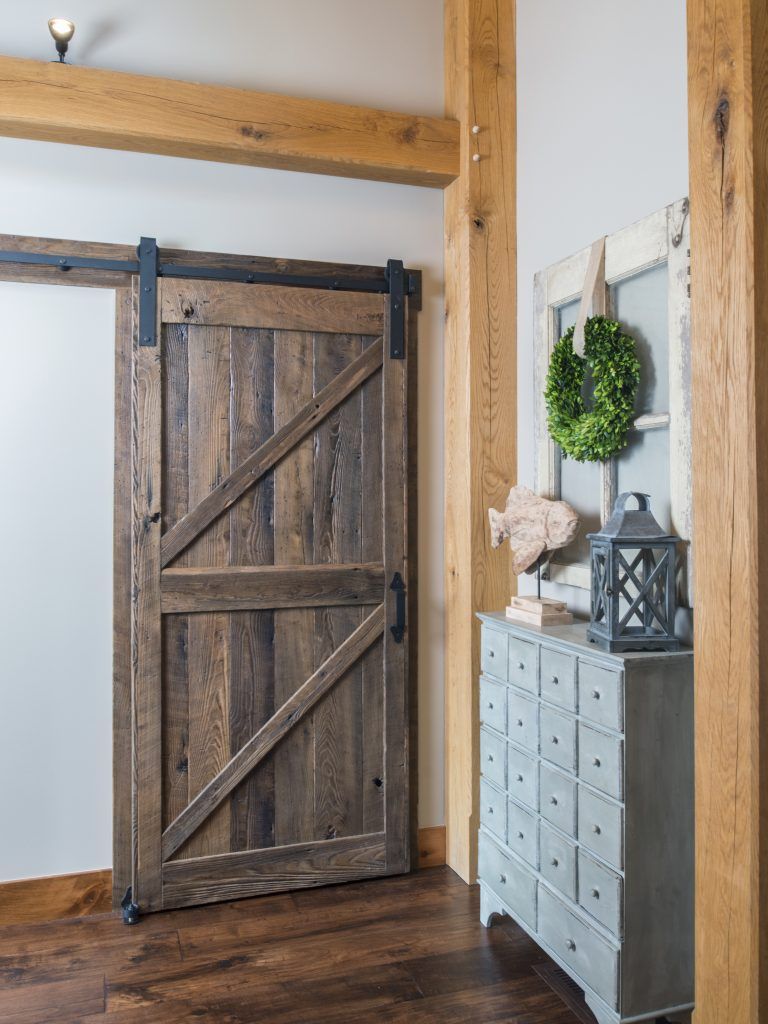 A wooden sliding barn door is in a room next to a dresser.