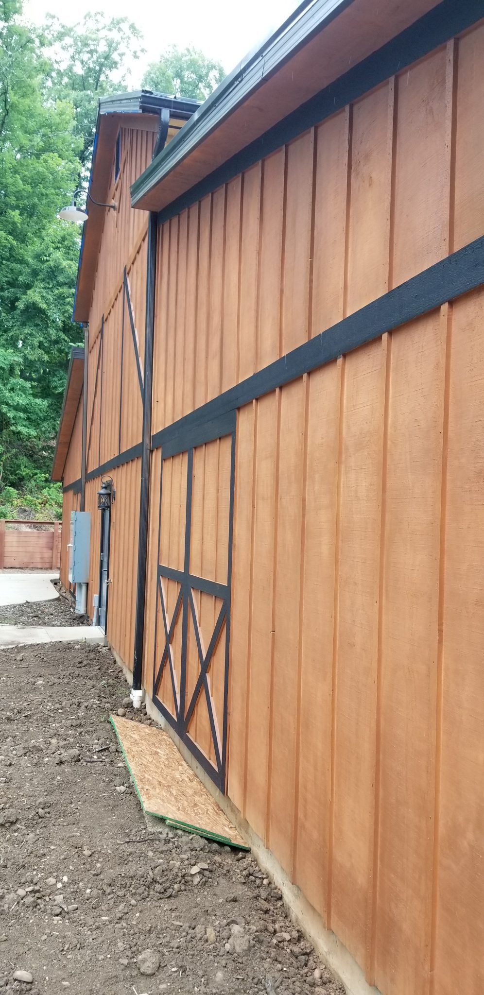 The side of a barn with a black trim and a door.