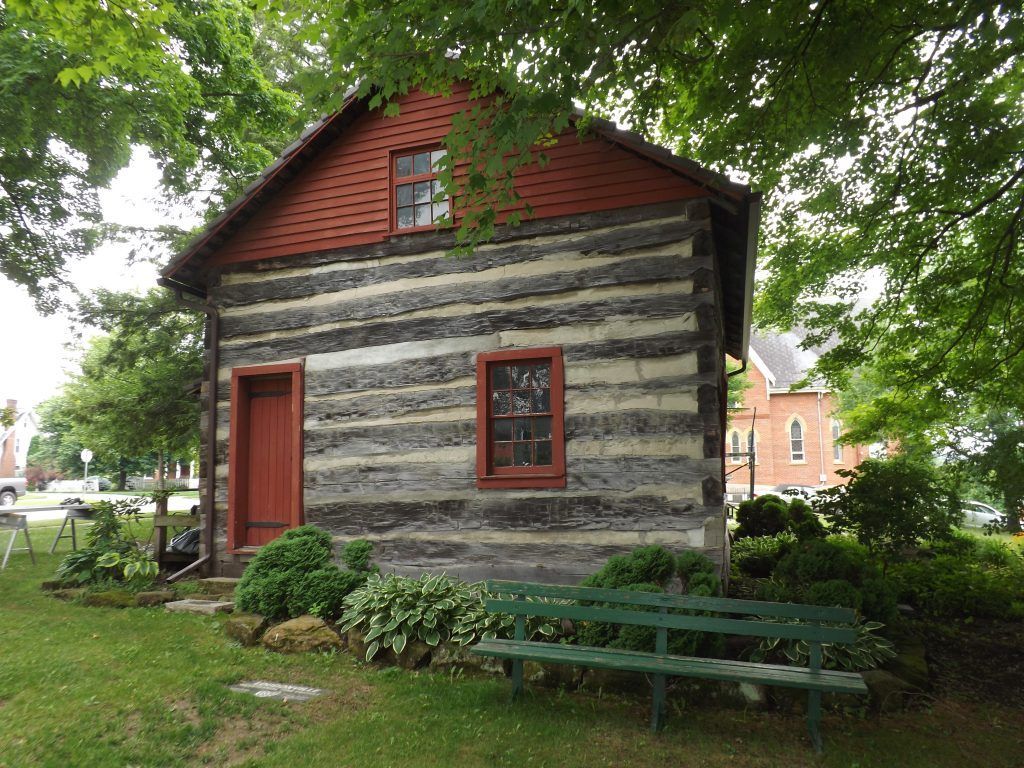 A small log cabin with a red roof and a green bench in front of it.