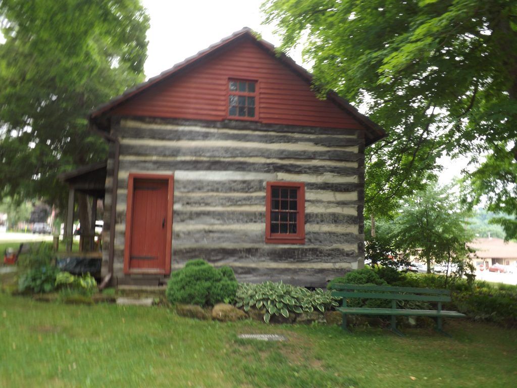 A small log cabin with a red door and a green bench in front of it