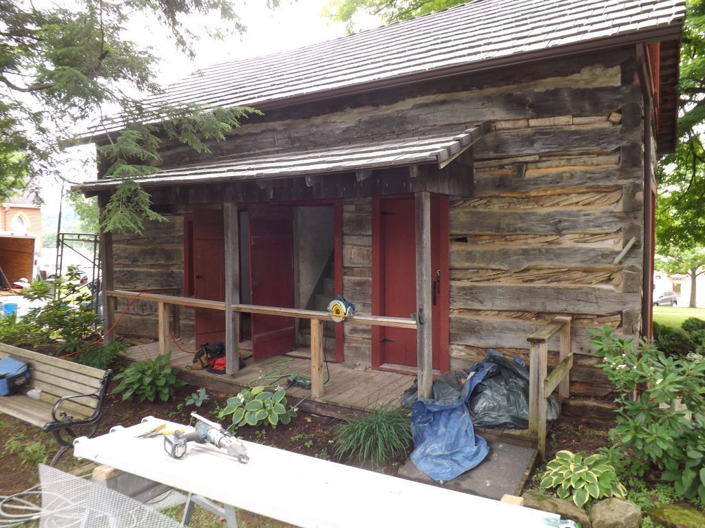 A small log cabin with a porch and a table in front of it.