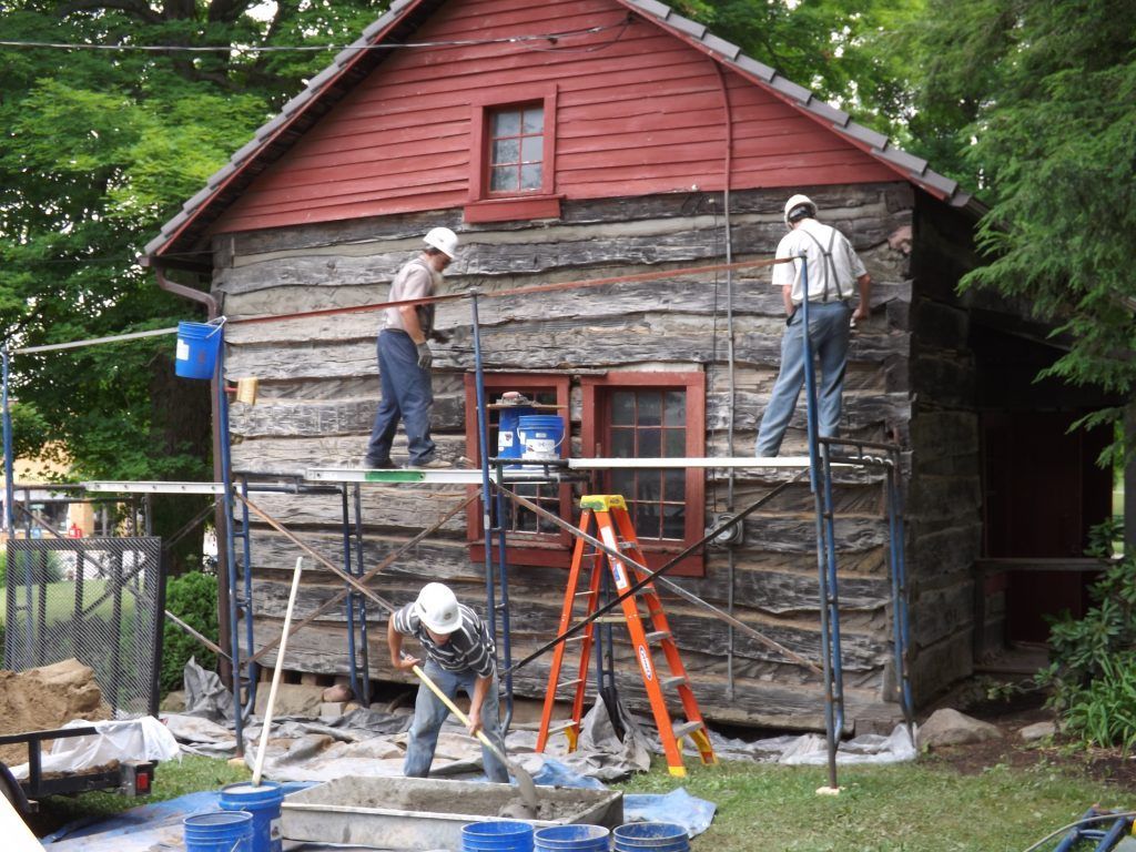 Two men are painting the side of a log cabin.