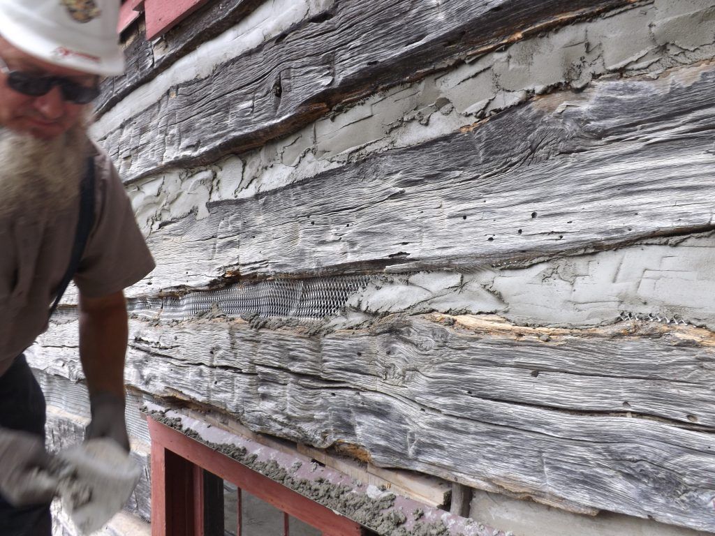 A man with a beard is working on a log cabin.