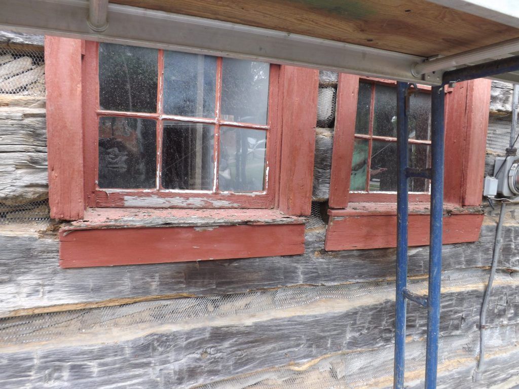 A log cabin with a red windows and a scaffolding.