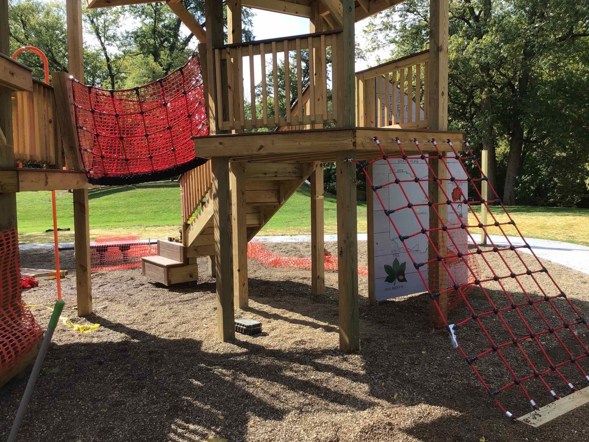 A wooden playground with stairs and a rope bridge in a park.