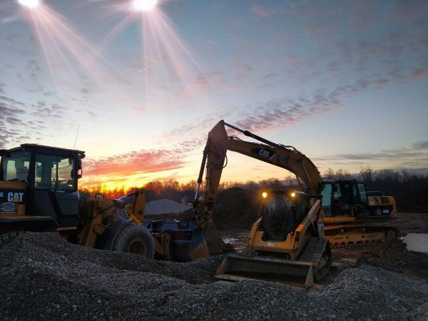 A cat excavator is working on a construction site at sunset.
