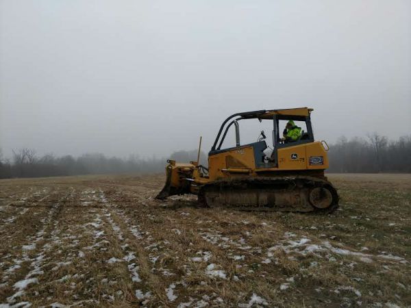 A man is driving a bulldozer in a field on a foggy day.