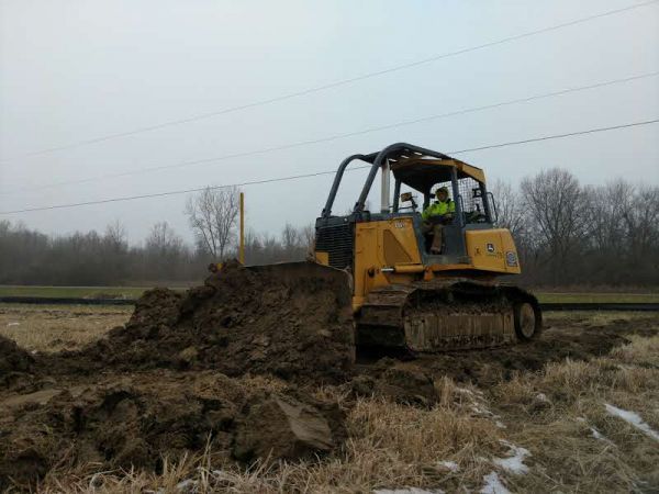 A man is driving a yellow bulldozer in a field.