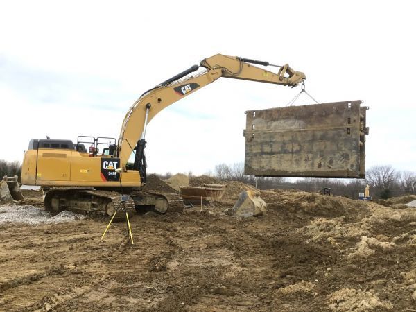A large yellow excavator is lifting a large concrete block in a dirt field.