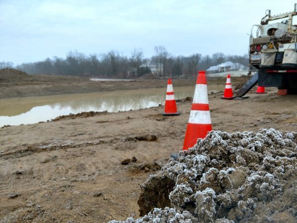 Orange and white traffic cones are sitting in the dirt near a body of water