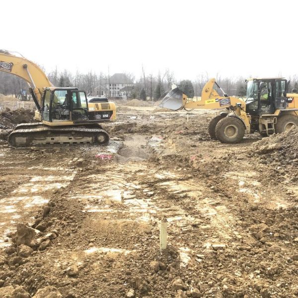 Two construction vehicles are driving through a muddy job site.