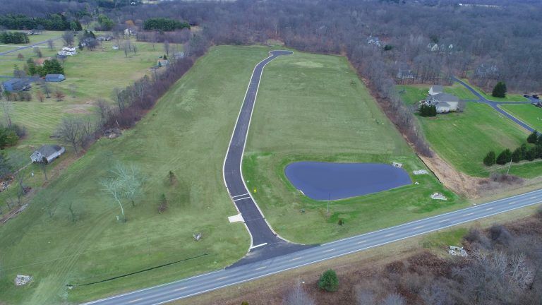 An aerial view of a residential area with a road and a pond.