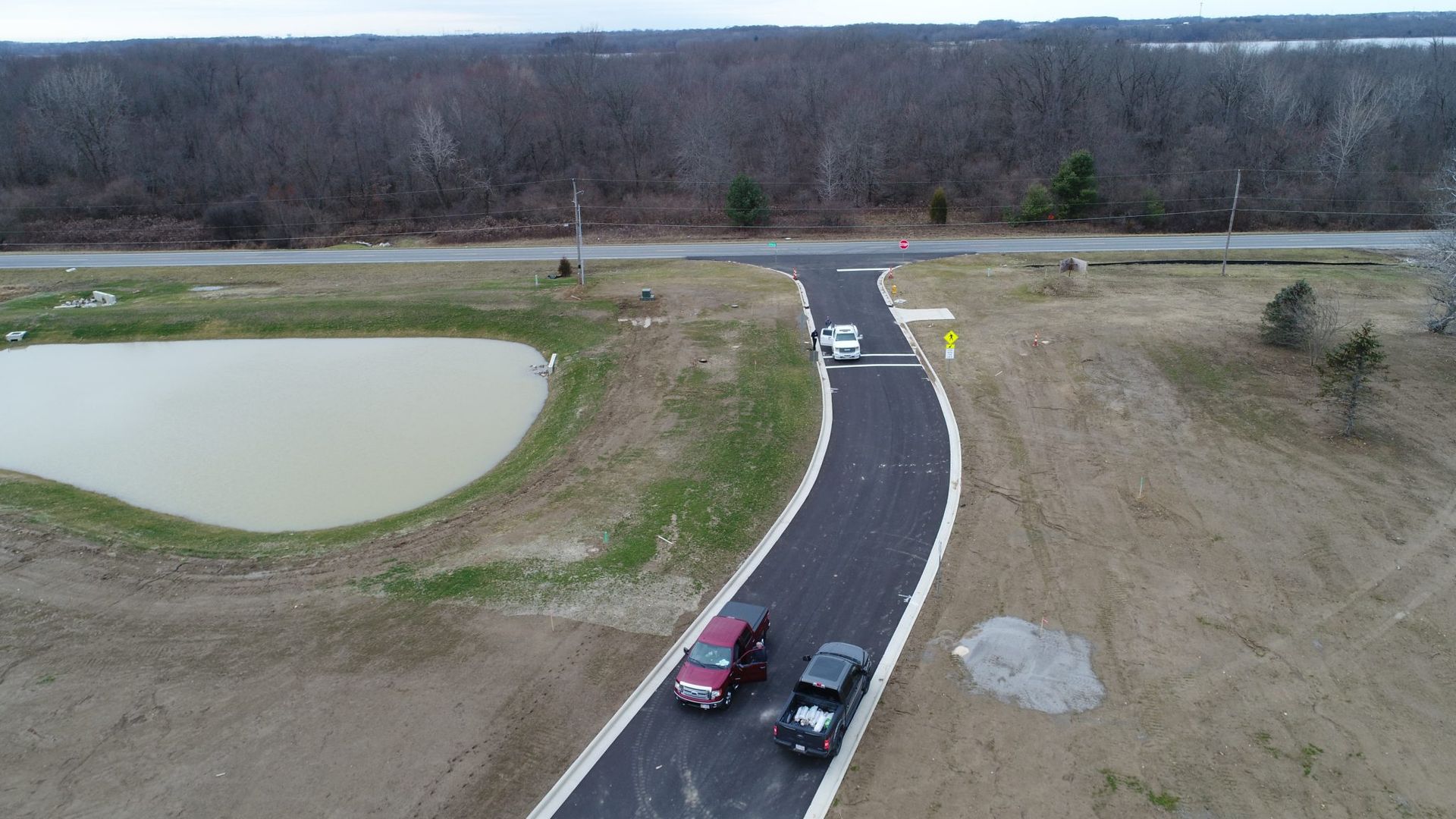 An aerial view of two cars driving down a road next to a pond.