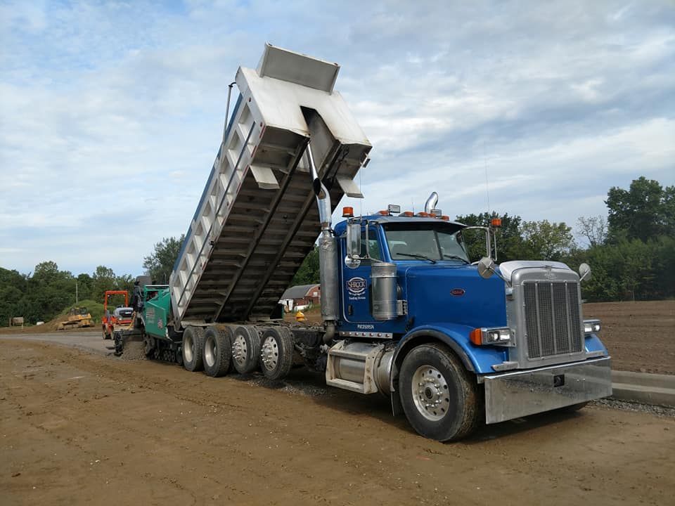 A blue dump truck is parked in a dirt field.