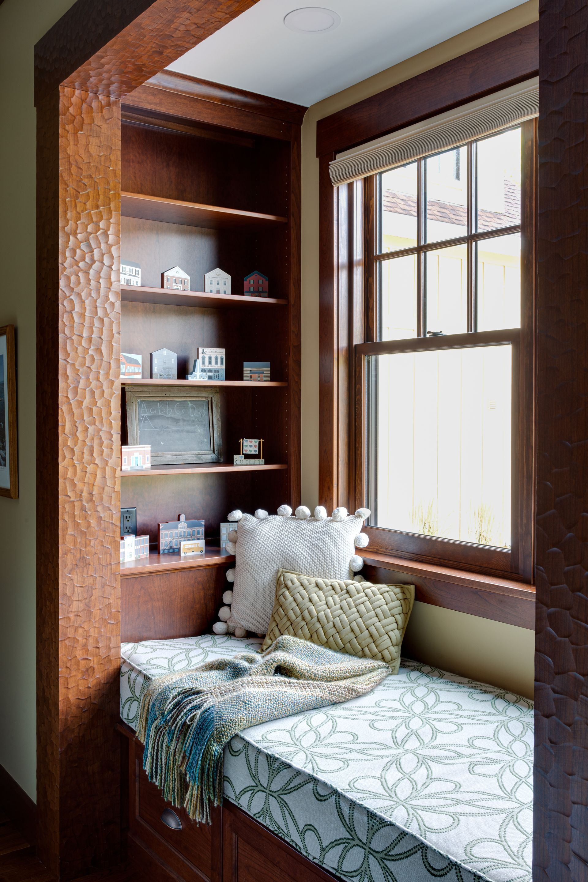 A corner of a room with a window seat and shelves.