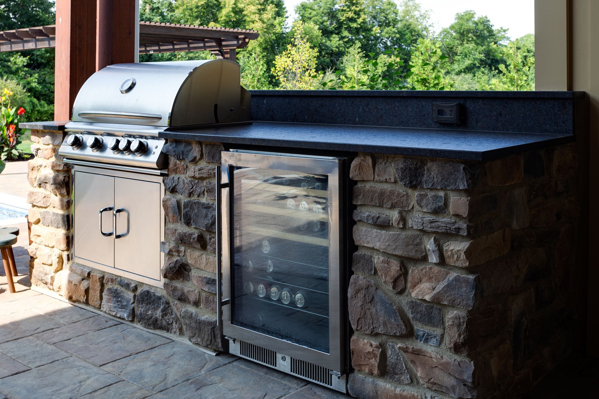 An outdoor patio kitchen with a grill and a refrigerator.
