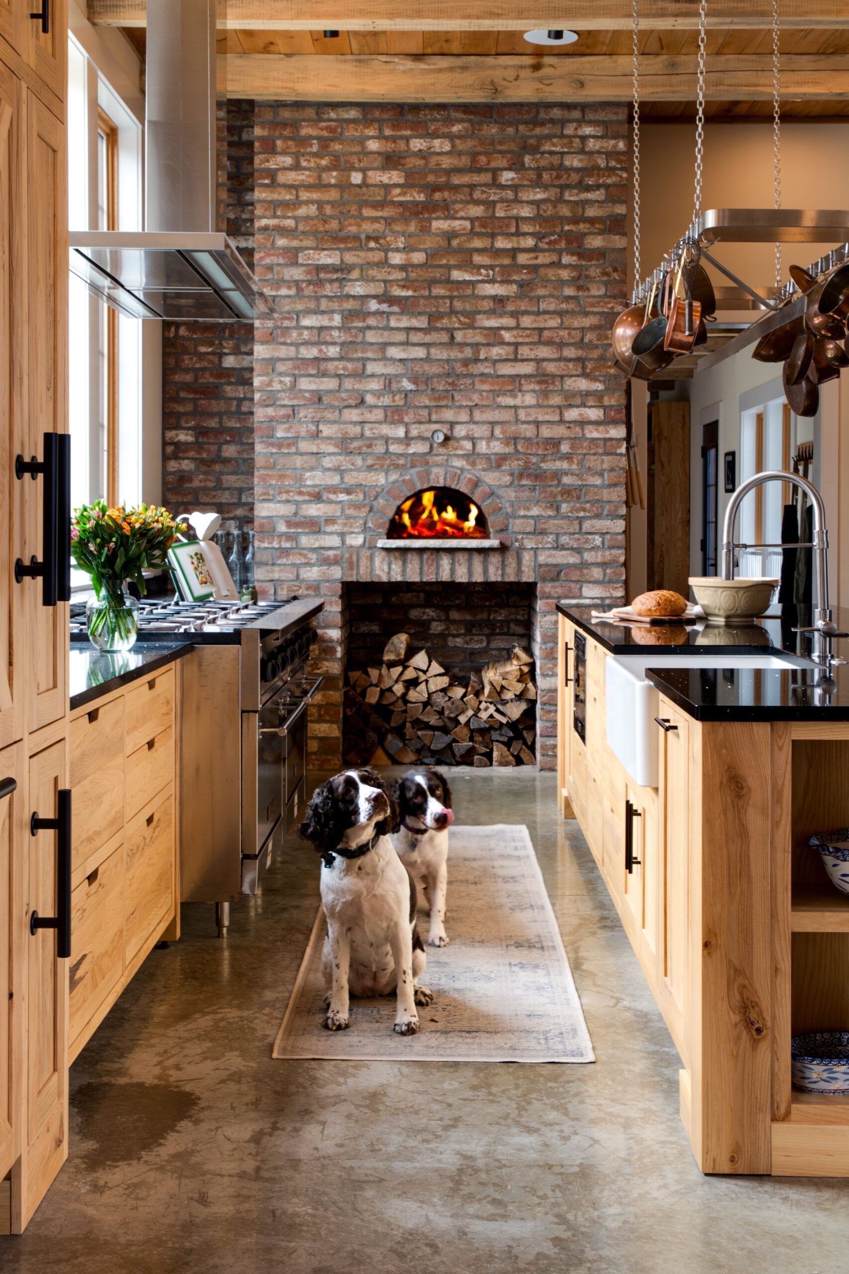 Two dogs are standing in a kitchen next to a brick fireplace.