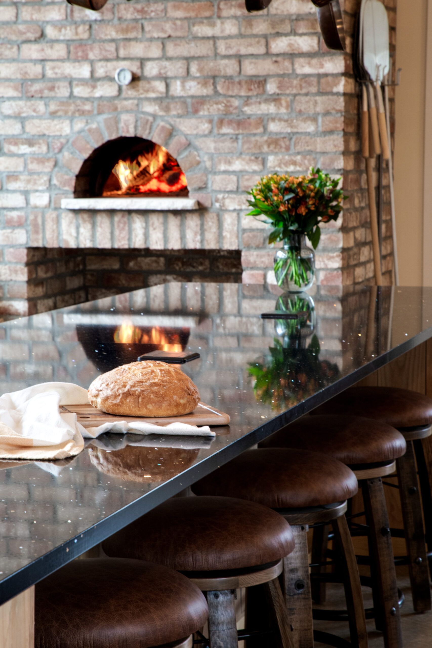 A brick oven is behind a counter with a loaf of bread on it.