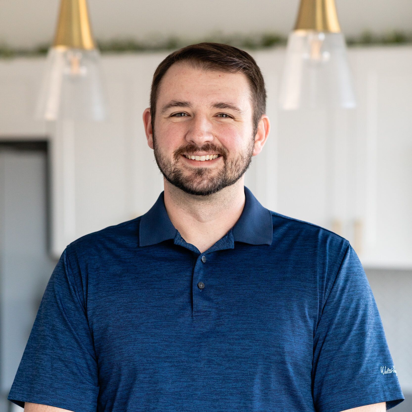 A man with a beard is wearing a blue polo shirt and smiling.