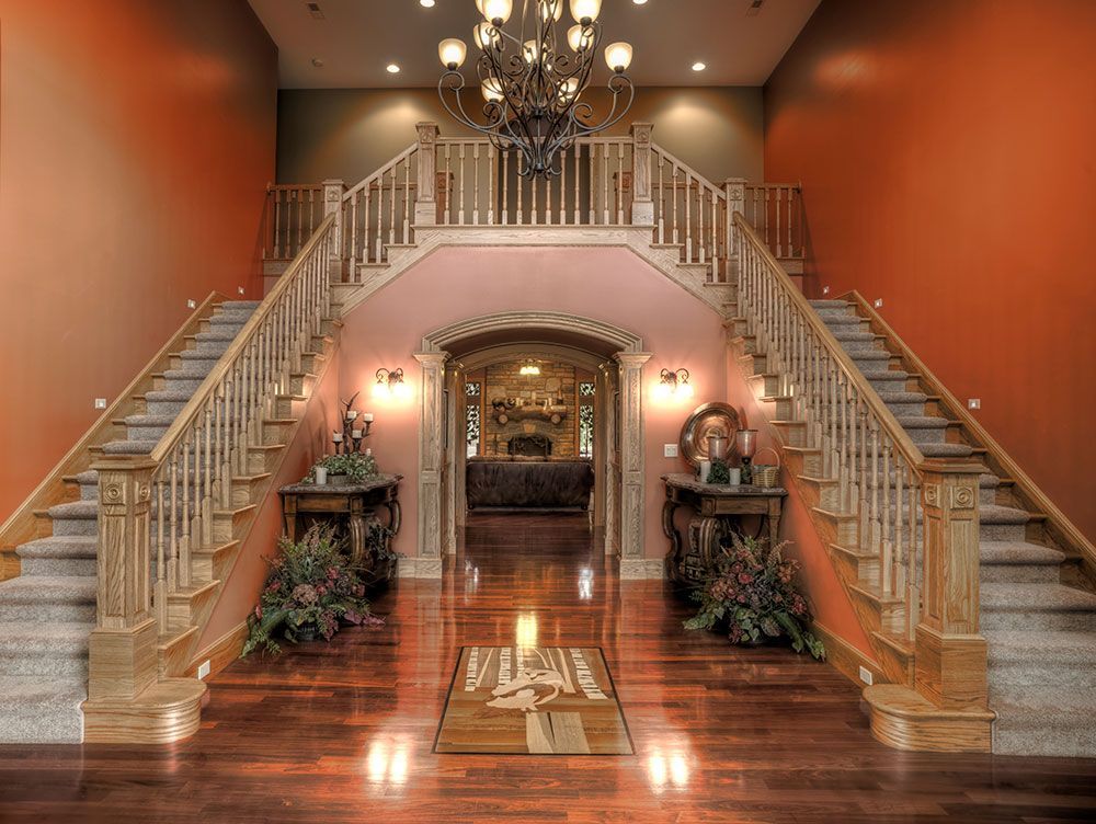 A large hallway with dual stair cases, hardwood floors, and a chandelier.