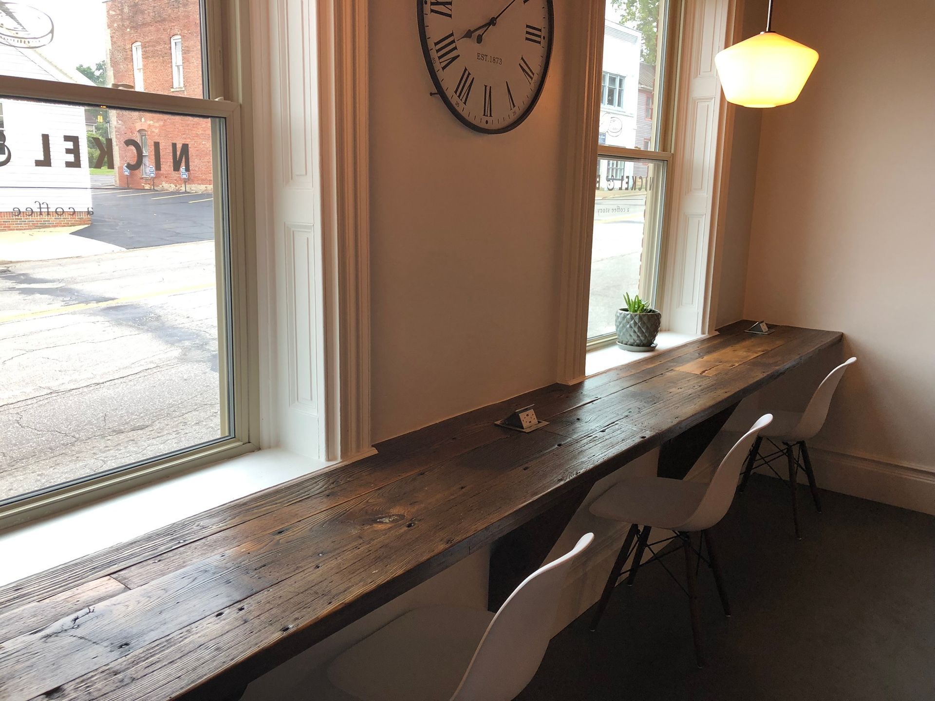 A clock hangs above a long wooden table in a room.